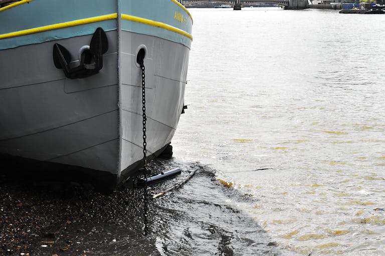 Close-up of a moored boat with chain and anchor on a calm river shoreline.